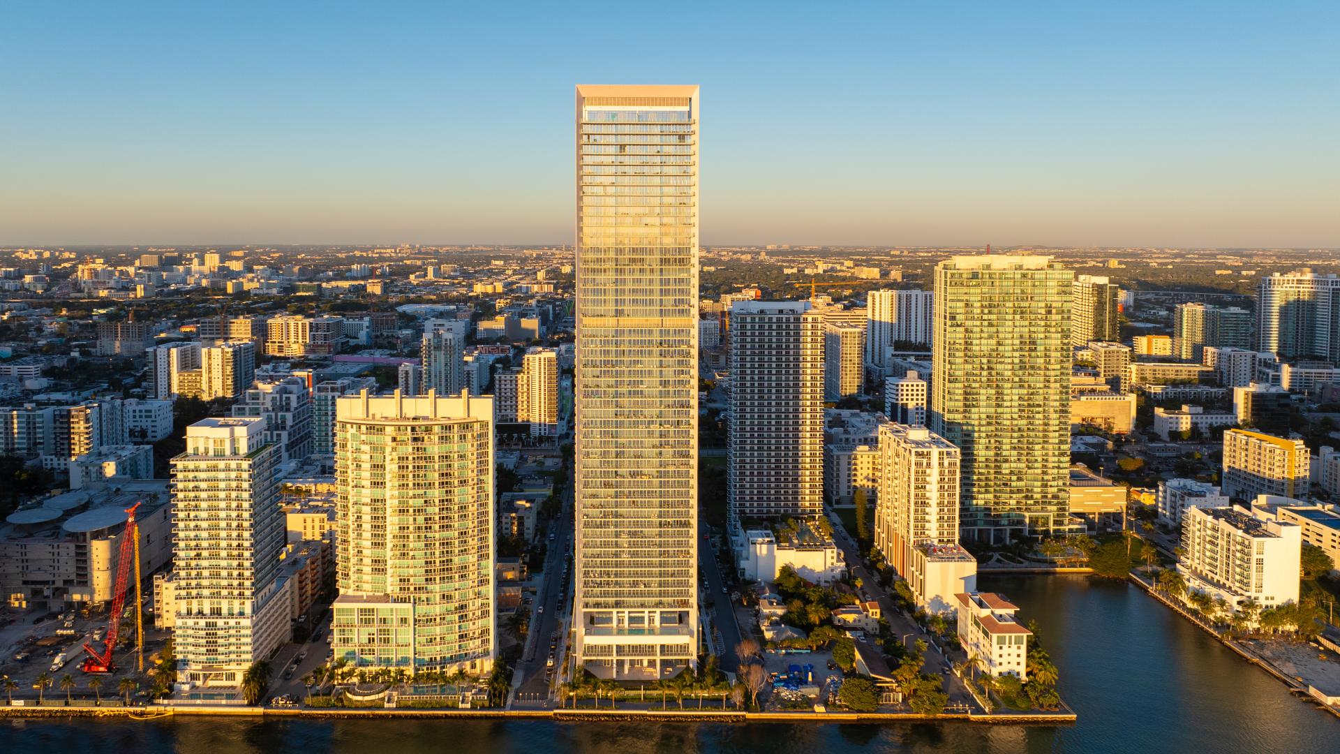 Aerial view of a tall, modern high-rise surrounded by smaller buildings.