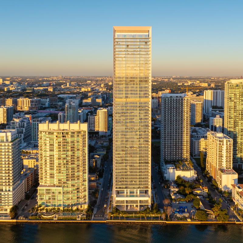 Aerial view of a tall, modern high-rise surrounded by smaller buildings.